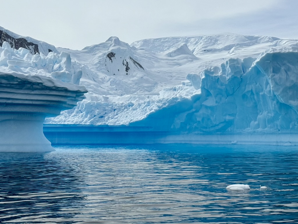 Sculpted layers of white ice beside an immense blue Antarctic ice wall