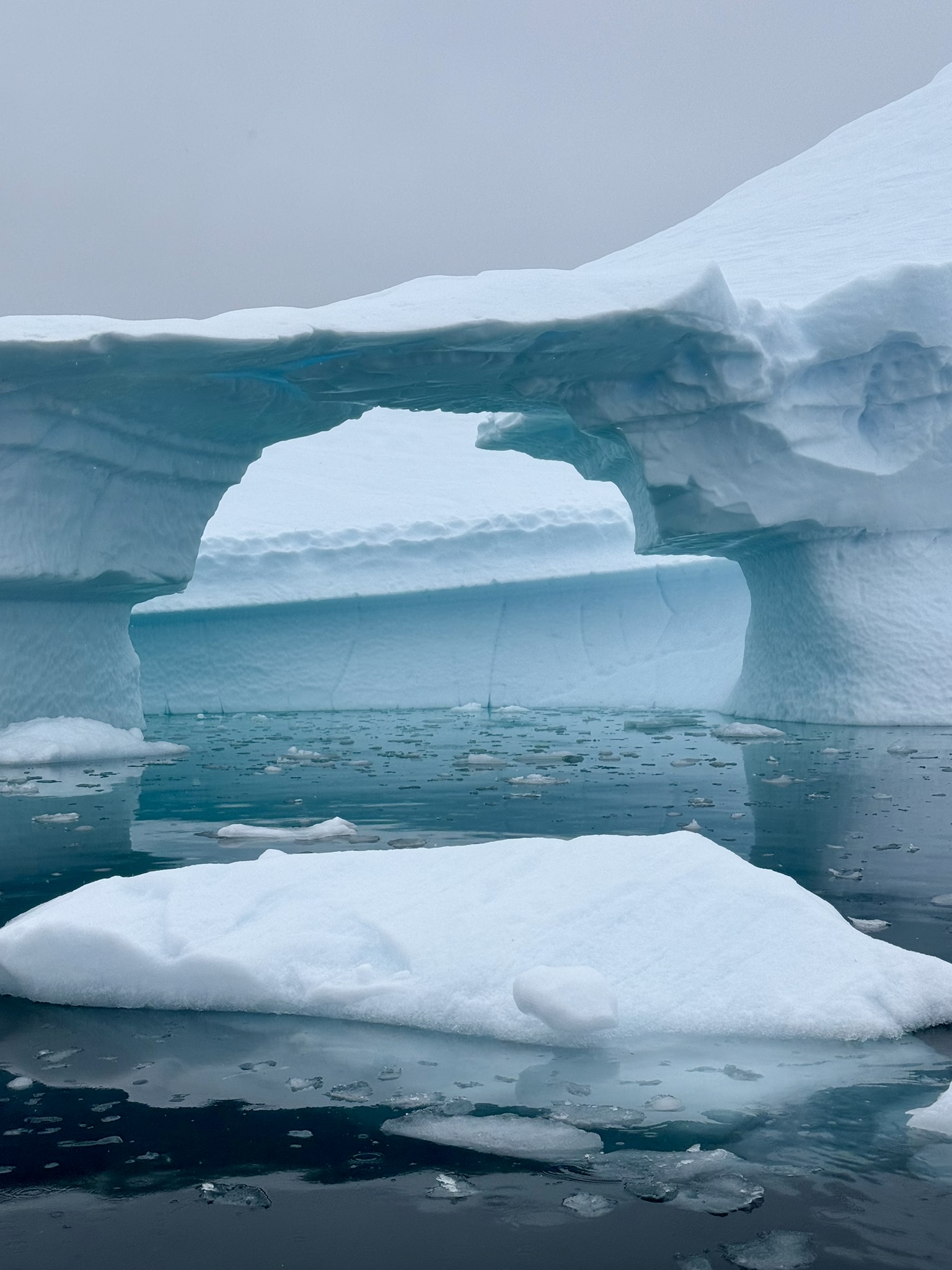 A natural arch carved into blue Antarctic ice above a turquoise inlet